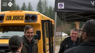 Group of people smiling and talking next to a school bus.